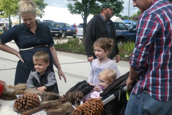 A young family checking out some North American animal hides and pine cones.